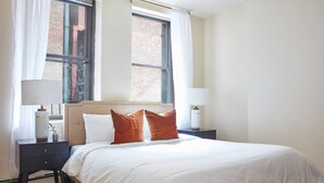 Een slaapkamer met een bed, twee nachtkastjes, een raam en een lamp op elk nachtkastje.