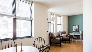 Une pièce comprenant une table de salle à manger ronde, deux chaises, un fauteuil marron, un bureau blanc et une lampe.