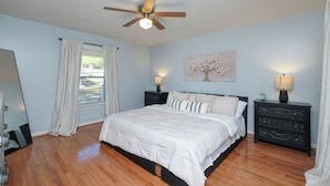A bedroom with a bed, two nightstands, a ceiling fan, a window with curtains, and a wall-mounted artwork. - large Stunning Retreat 15 min to Downtown Huntsville 3br/3bath (Huntsville)