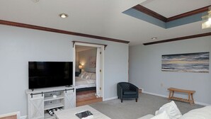 A living room with a TV, white sofa, and a painting on the wall. - large Stunning Retreat 15 min to Downtown Huntsville 3br/3bath (Huntsville)