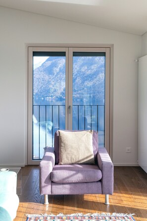Ein Zimmer mit einem violetten Sofa, Blick auf Berge durch eine Balkontür und Holzboden.