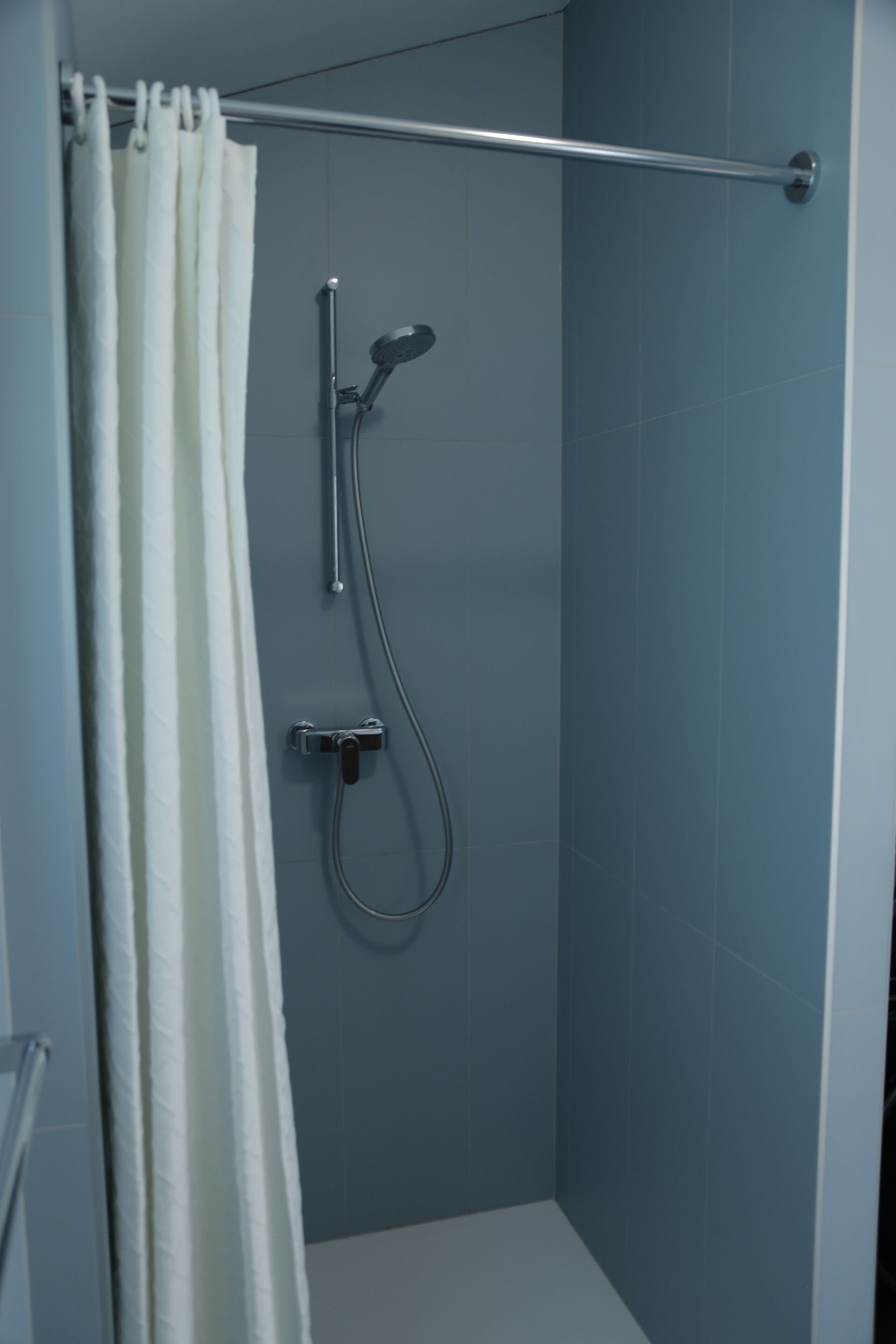 A shower with a curtain, a handheld showerhead, and a wall-mounted faucet.