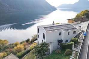 Ein modernes Gebäude mit flachem Dach, in der Nähe eines Gewässers mit Bergen im Hintergrund.