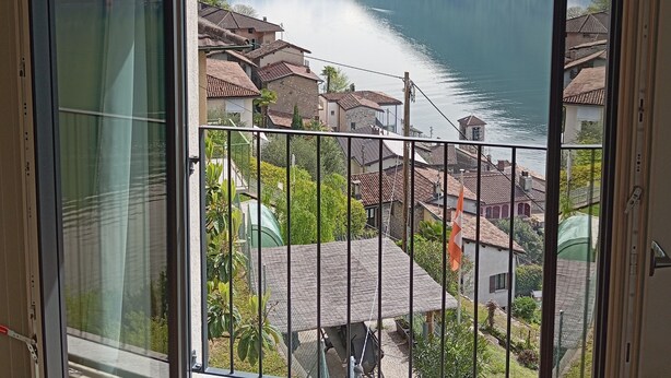 Una stanza con un'ampia porta scorrevole in vetro che si apre su un balcone con vista su un lago e montagne.