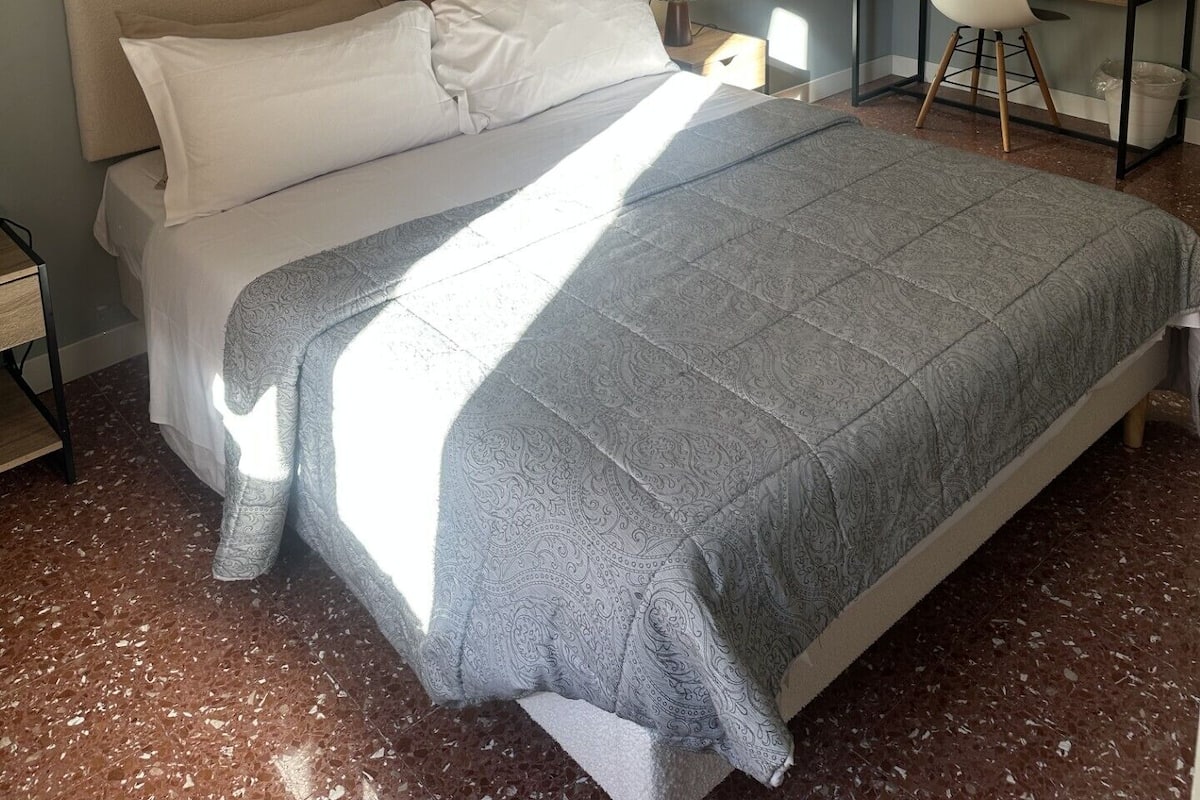 Ein ordentlich eingerichtetes Schlafzimmer mit Bett, Nachttisch, Lampe und Schreibtisch mit Stuhl.