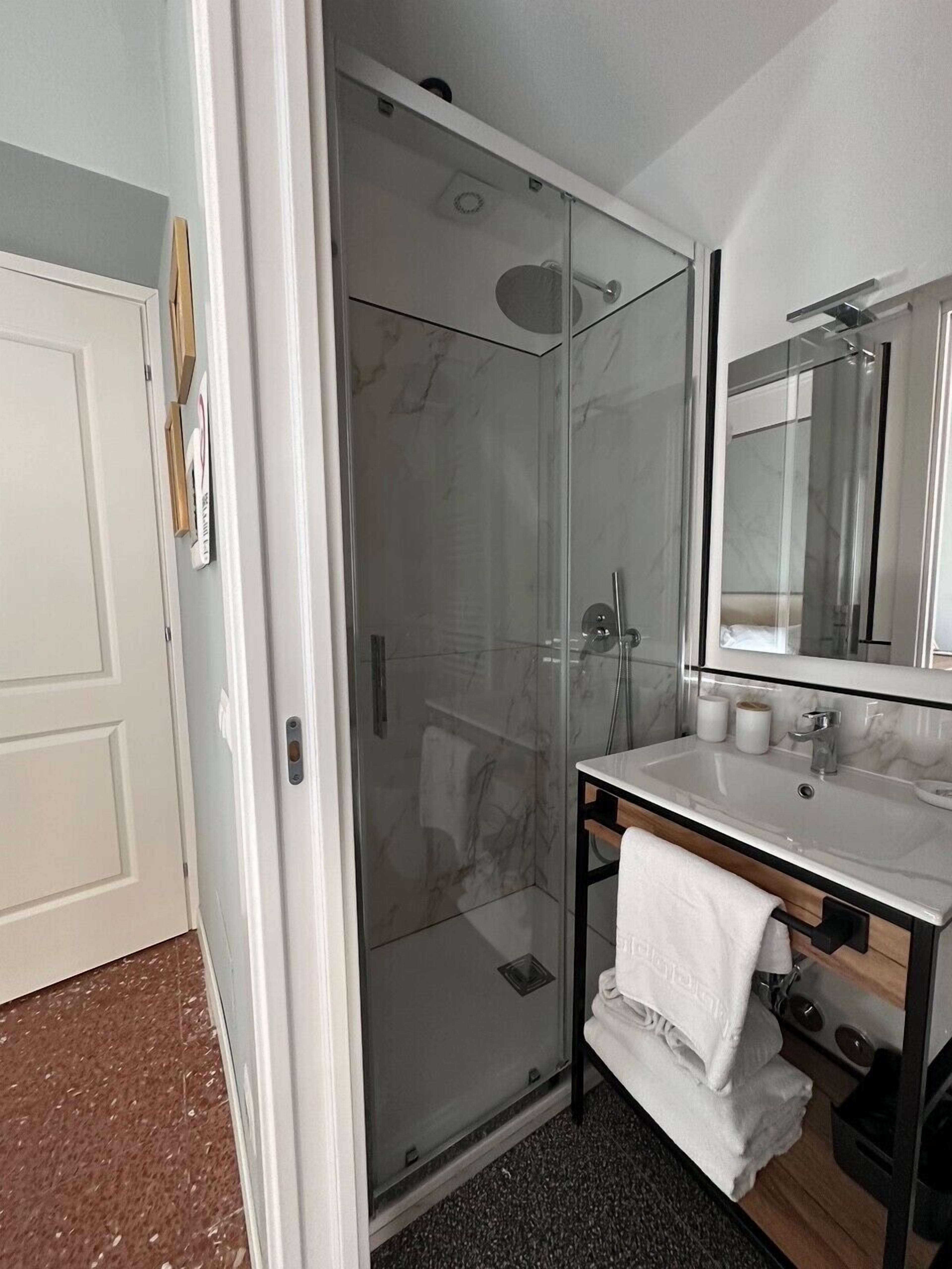 A modern bathroom with a glass-enclosed shower, a vanity with a mirror, and a towel rack.