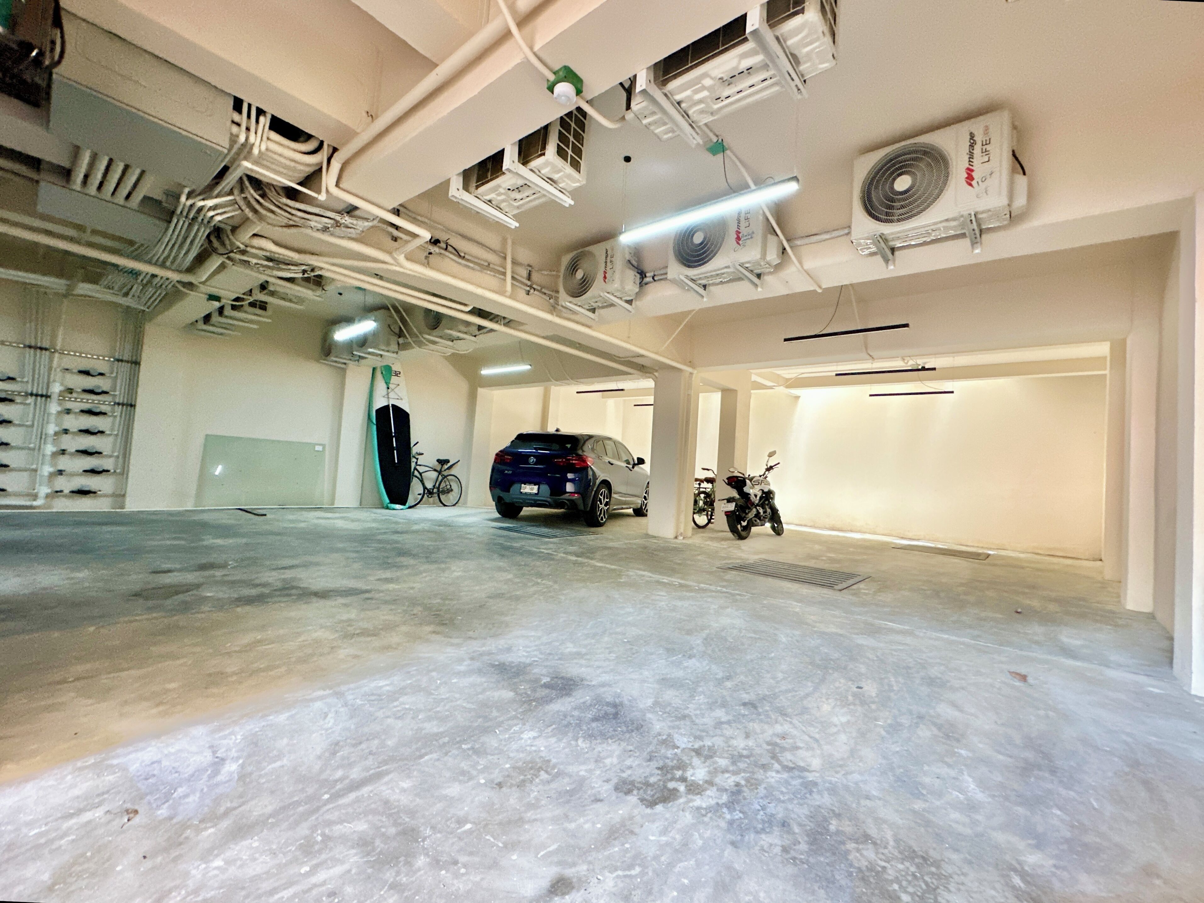 Un parking avec des planchers en béton, plusieurs unités de climatisation et quelques véhicules stationnés, dont une voiture et une moto.