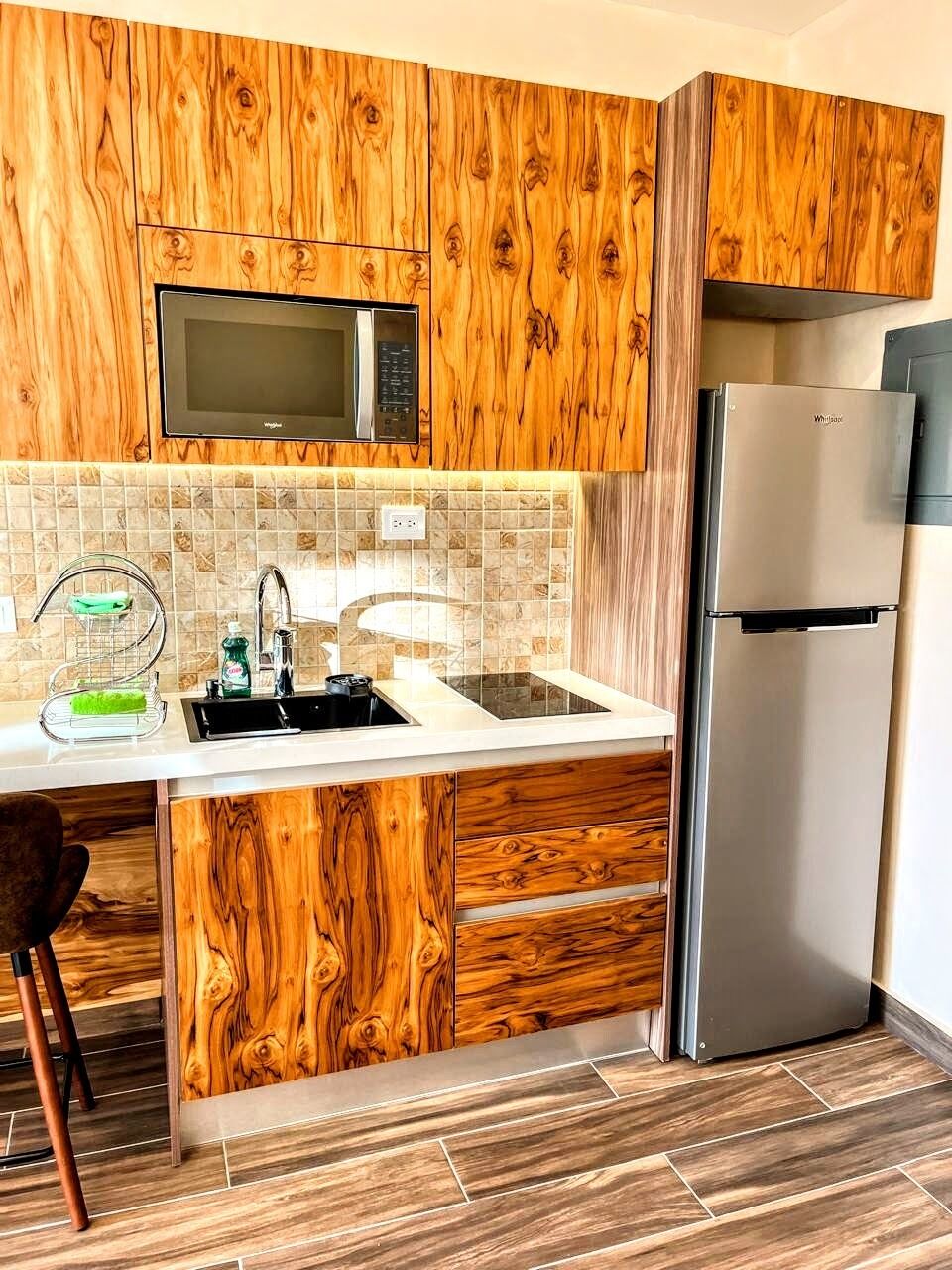 Una cocina con muebles de madera, un refrigerador de acero inoxidable, un microondas y un lavamanos con un grifo moderno.