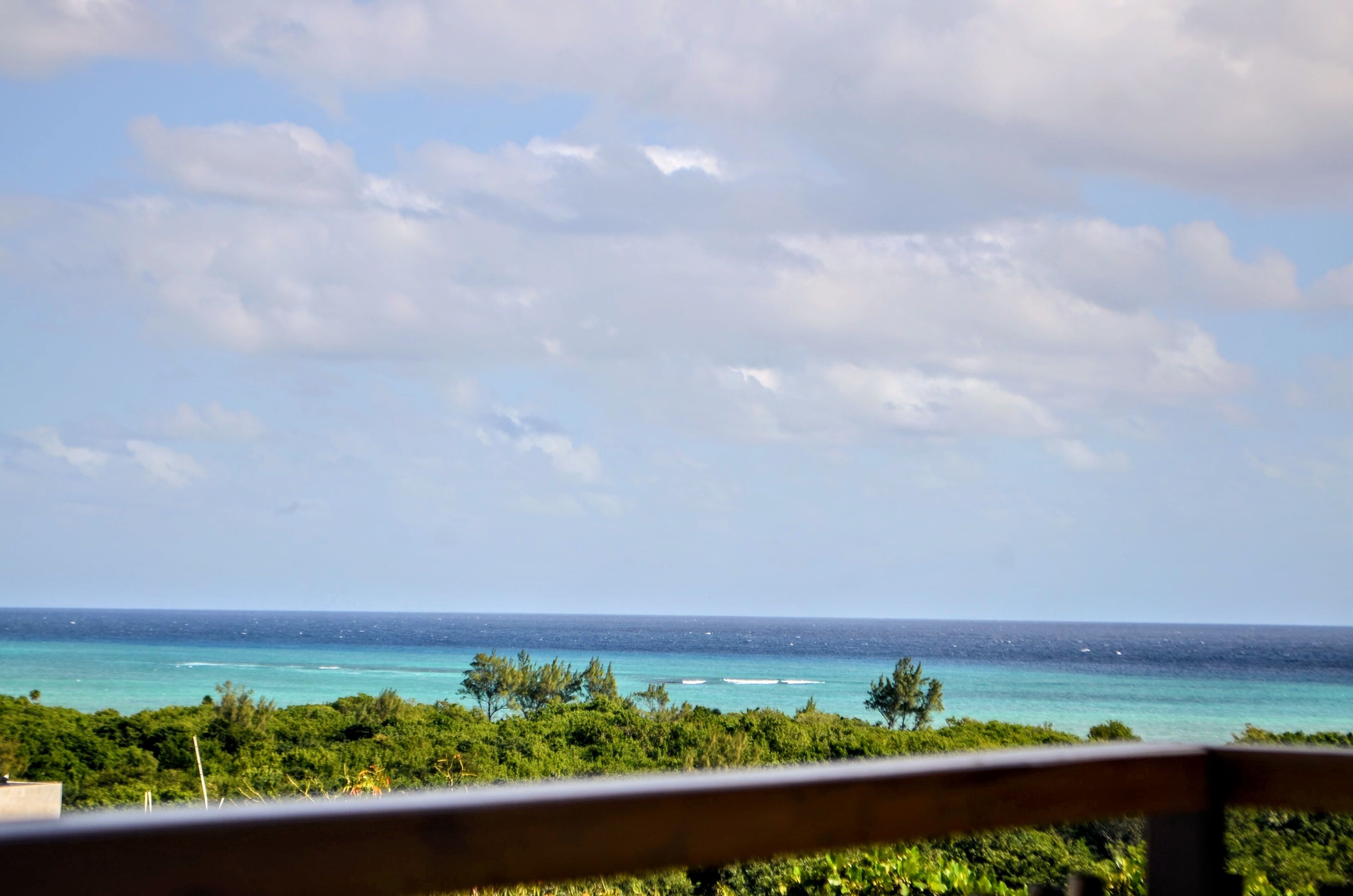 A view of the ocean from a balcony with a wooden railing.