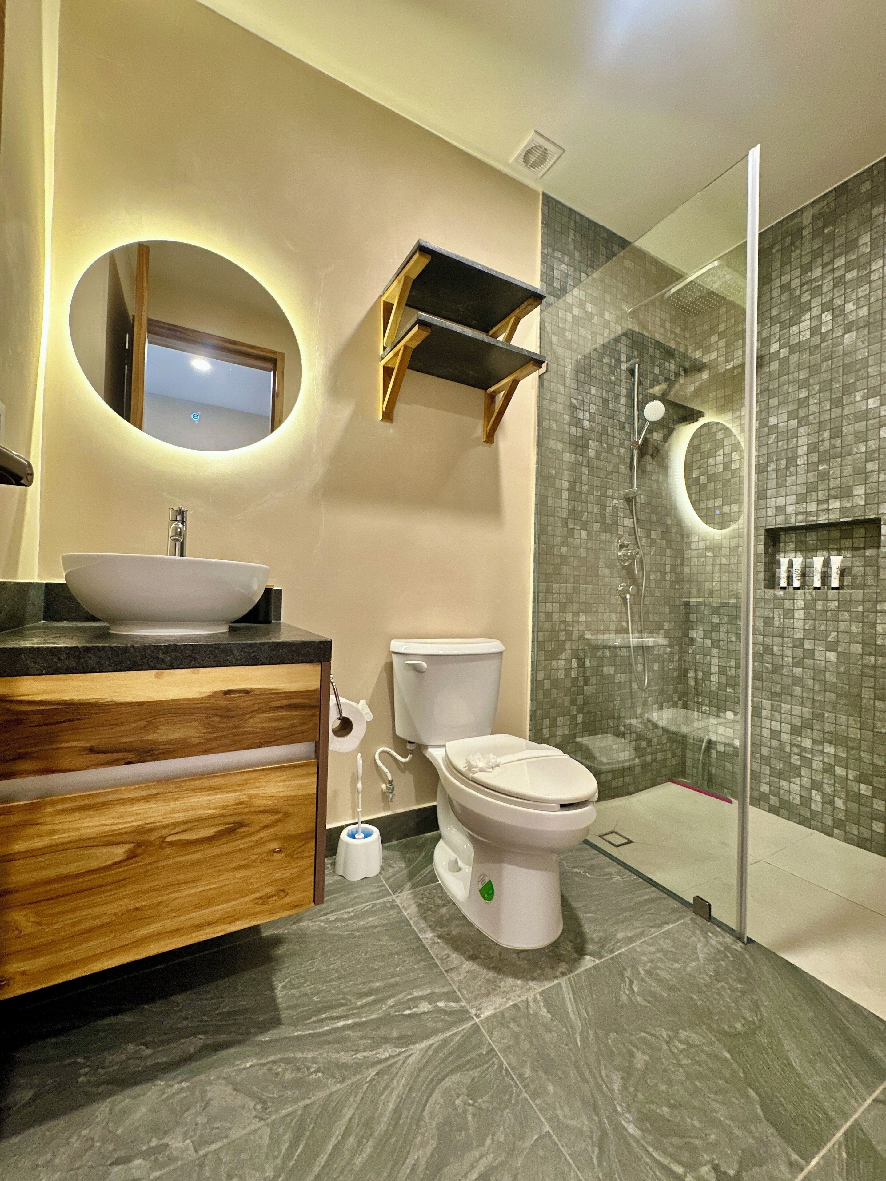 A modern bathroom with a round mirror, a sink, a toilet, and a glass-enclosed shower area.