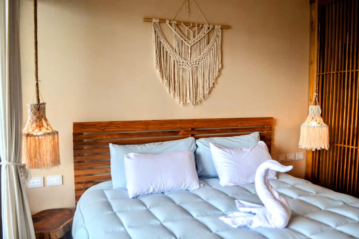 Un lit avec une tête de lit en bois, deux oreillers et une décoration murale en macramé au-dessus.