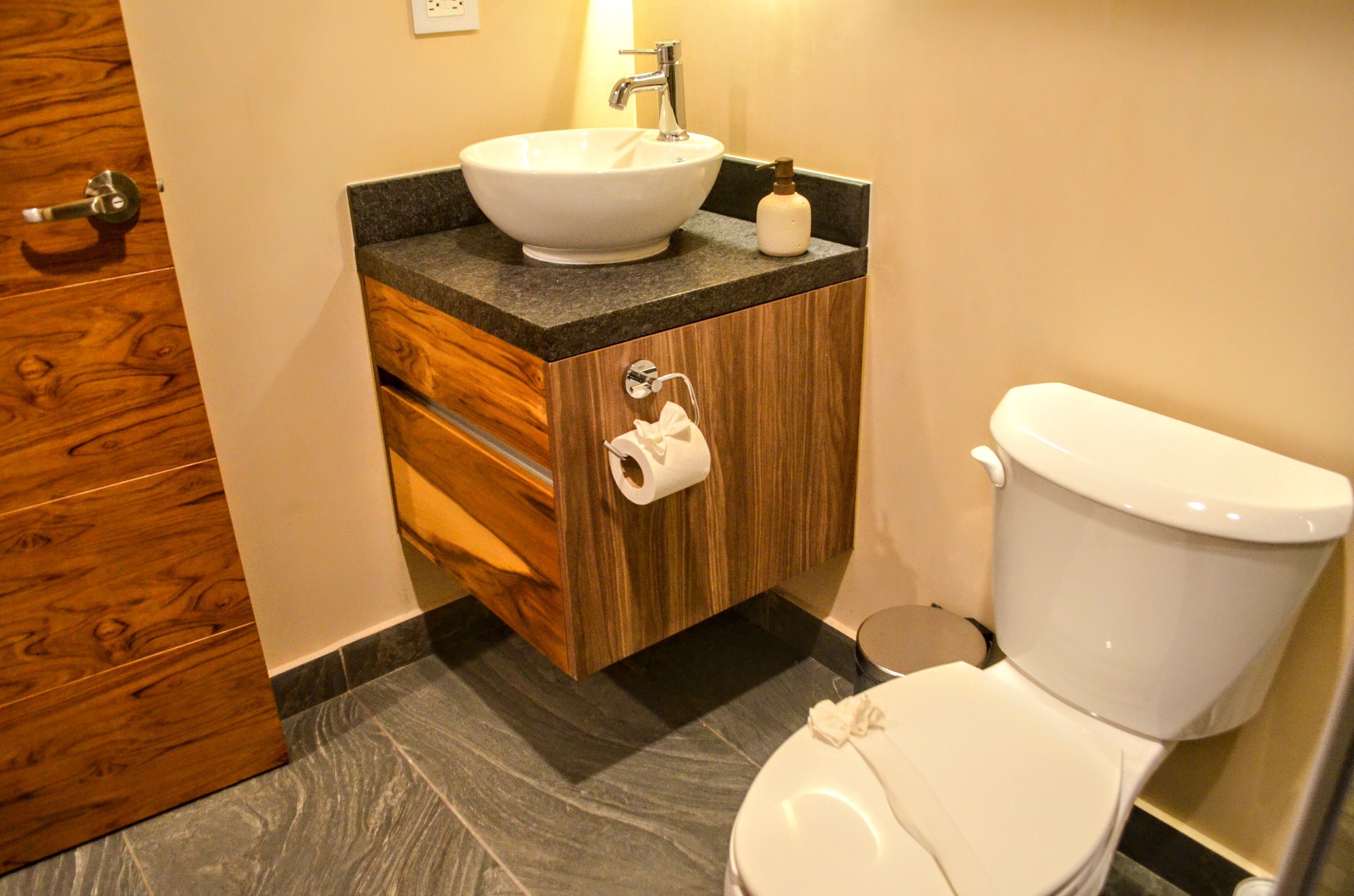 Un baño con tocador de madera, lavamanos blanco y retrete.