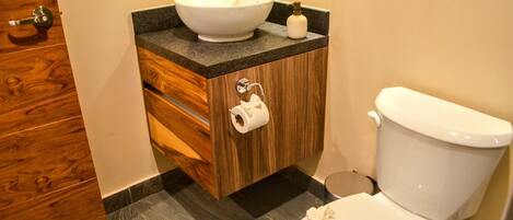 Un baño con tocador de madera, lavamanos blanco y retrete.