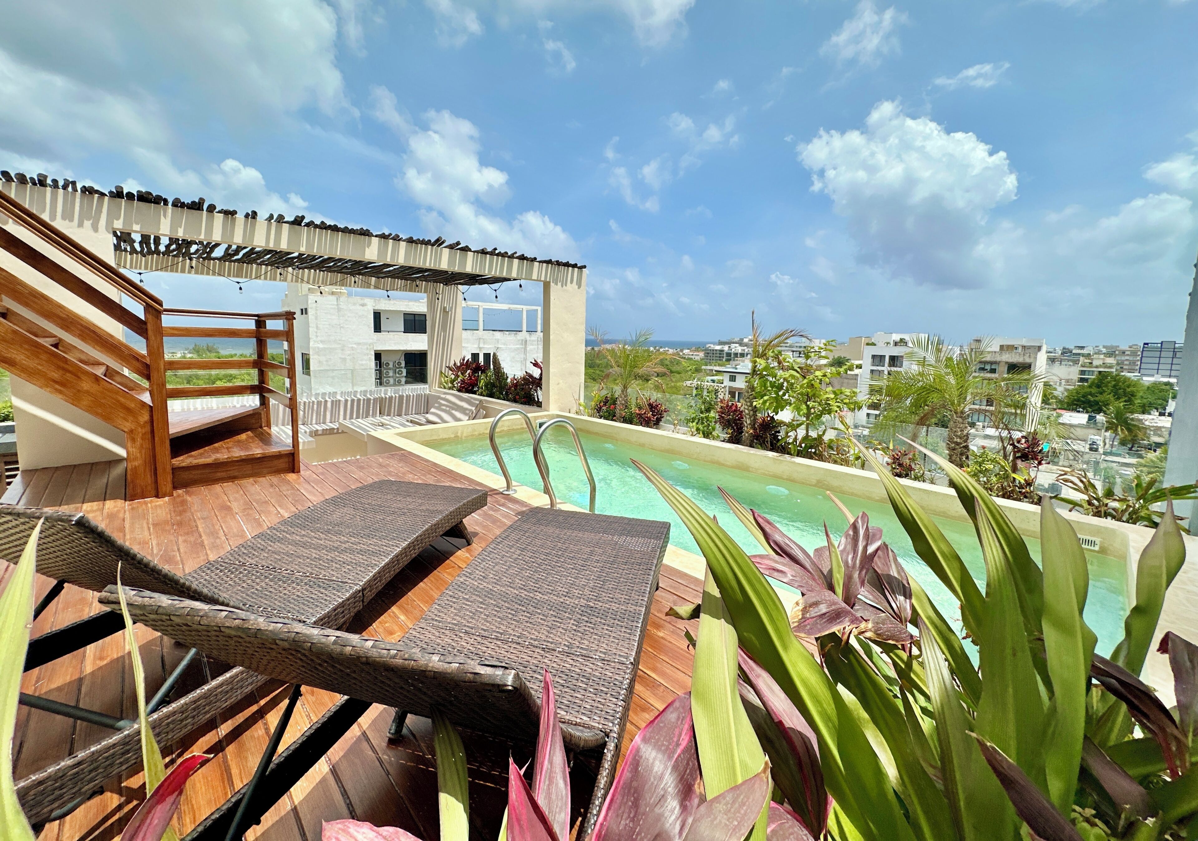 A rooftop pool area with lounge chairs, a wooden deck, and a view of the cityscape.