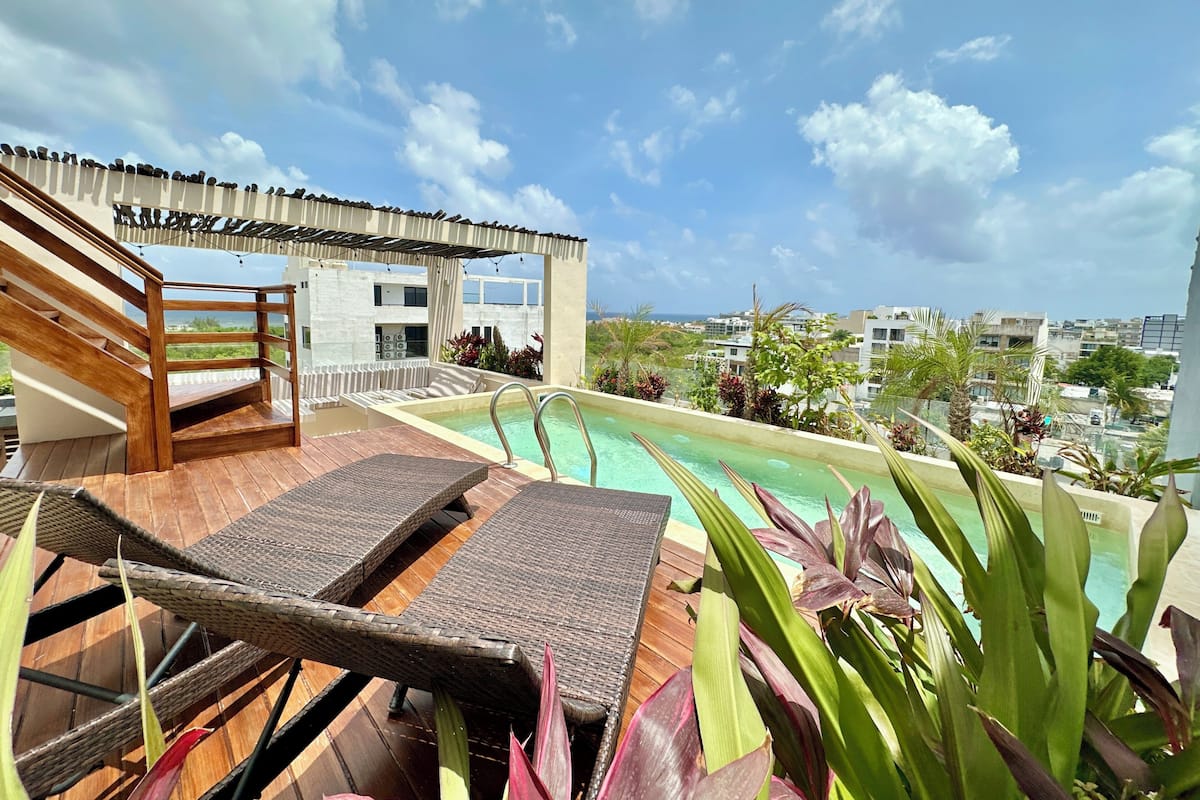 A rooftop pool area with lounge chairs, a wooden deck, and a view of the cityscape.
