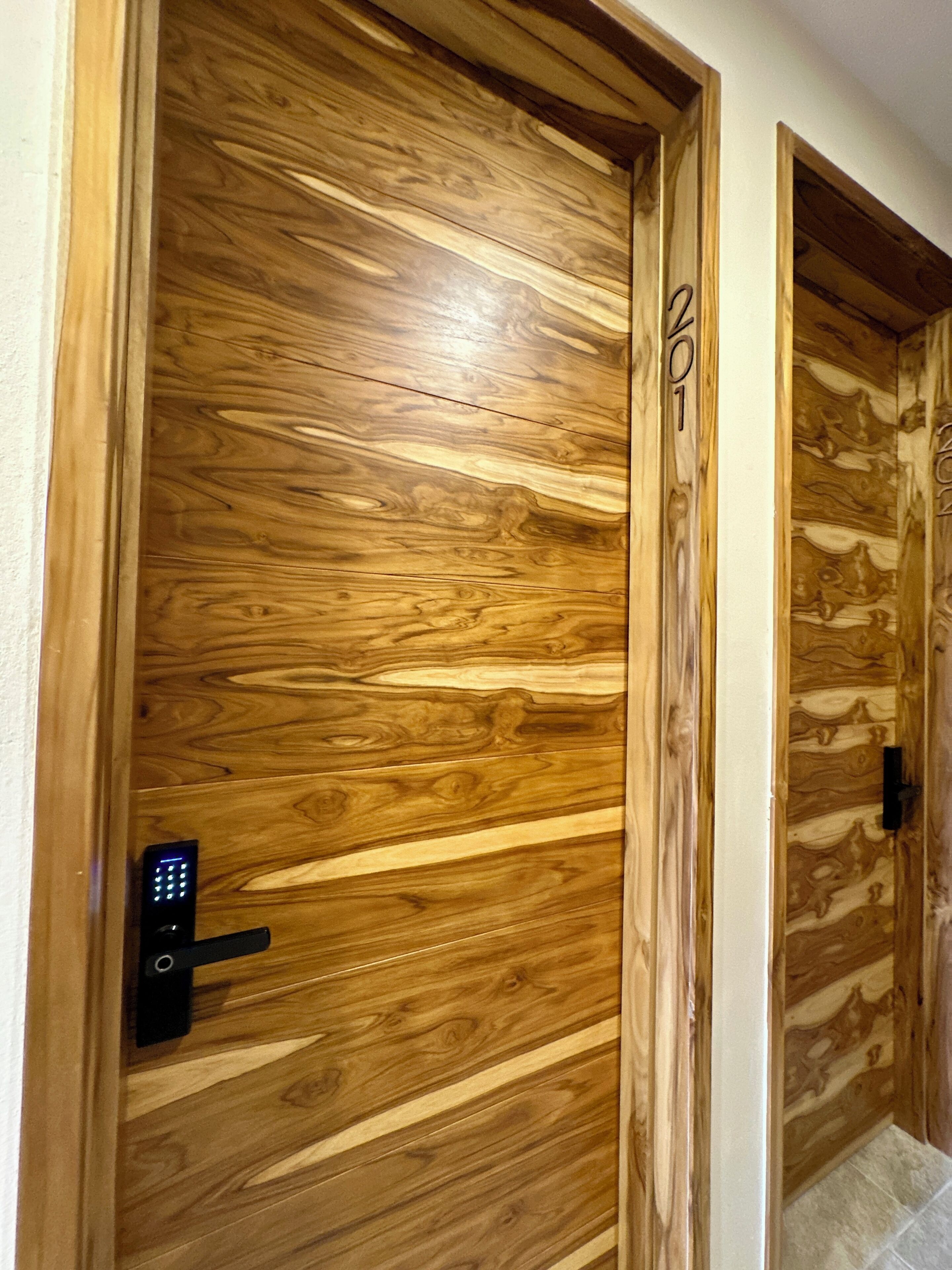 Una puerta de madera con cerradura electrónica, se ve el número '2' en la puerta, y una vista parcial de otra puerta con un diseño similar.