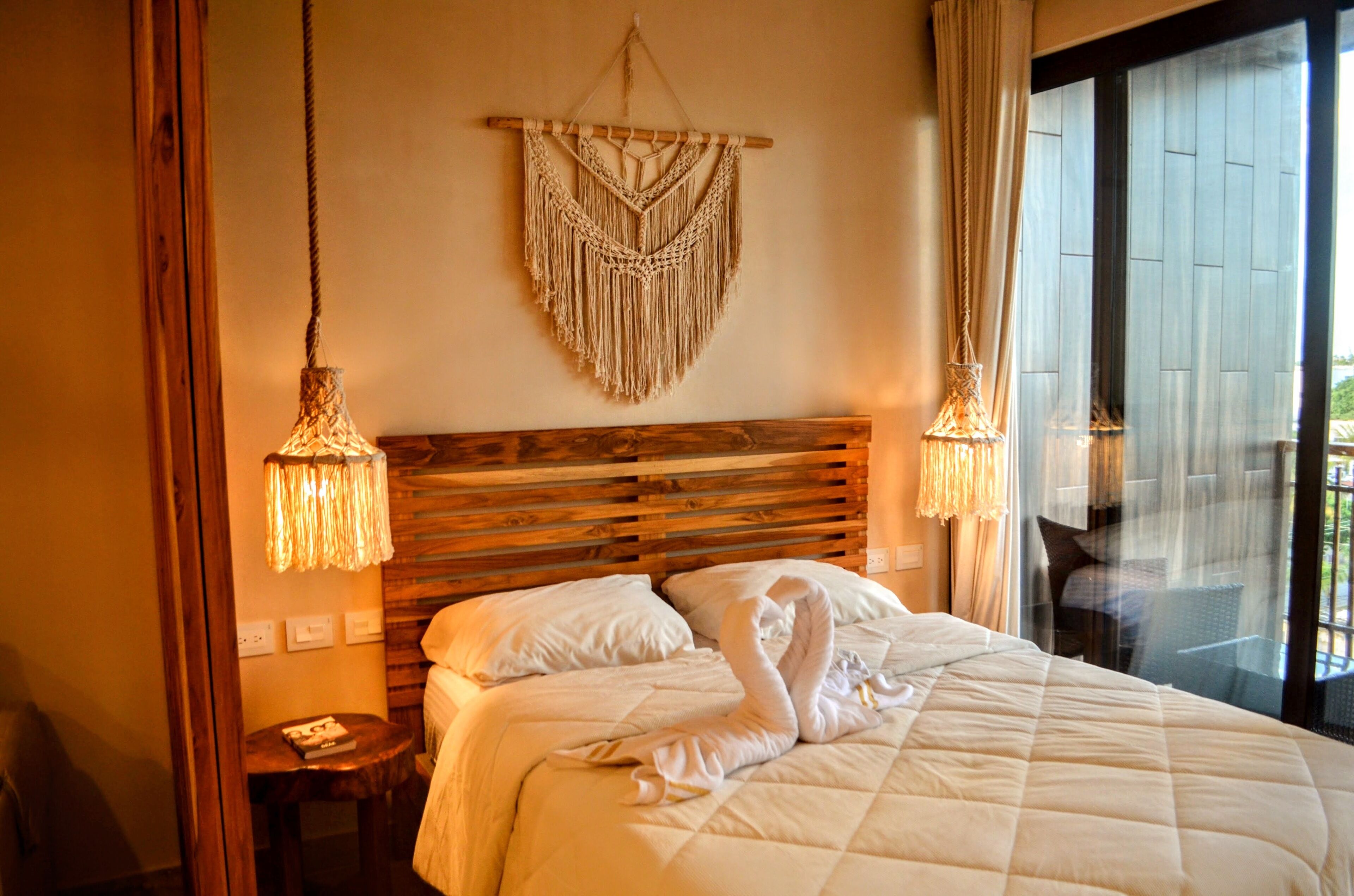 Ein Hotelzimmer mit einem hölzernen Kopfteil, einer Wanddekoration aus Makramee und einem Bett mit weißer Bettdecke.