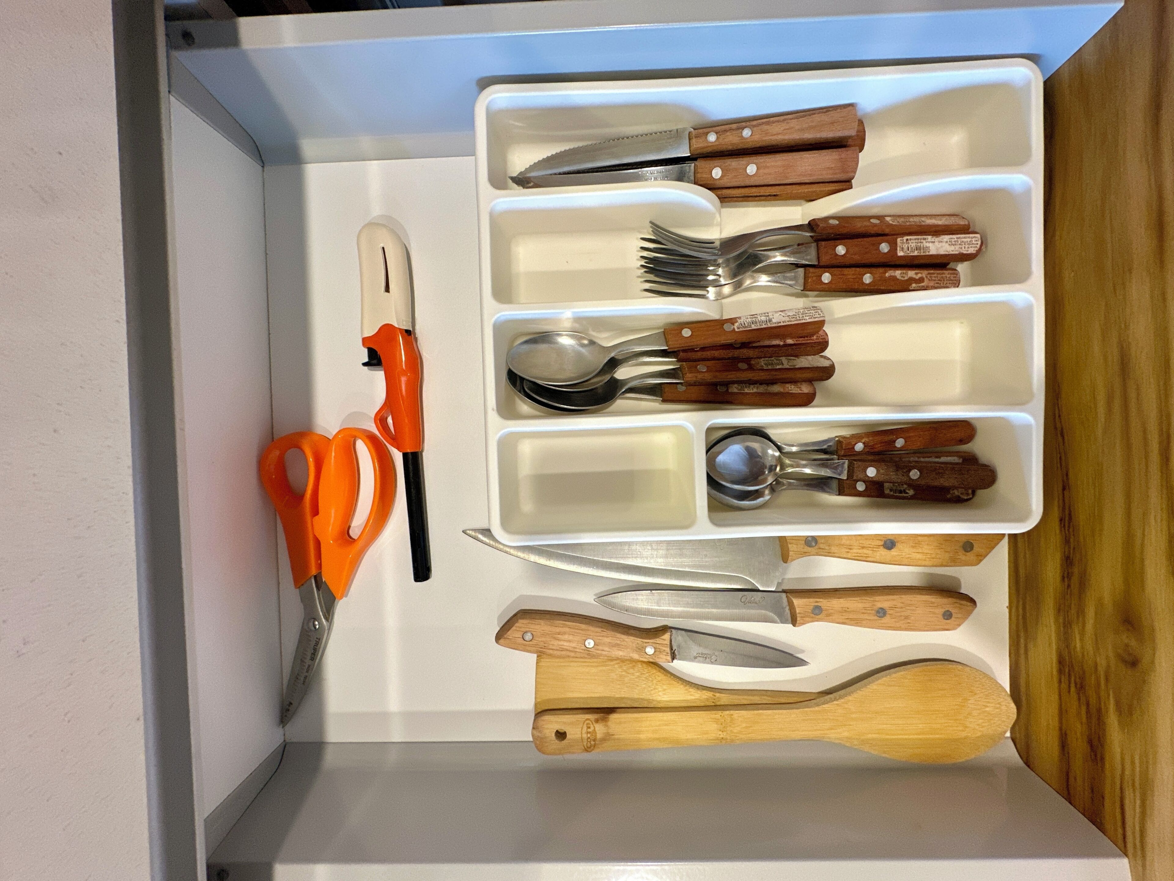 A drawer with various kitchen utensils, including knives, forks, and a pair of scissors.