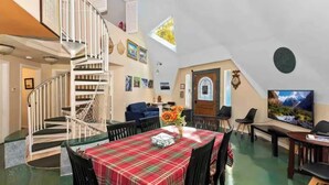 Uma sala de estar ampla com uma mesa de jantar, uma escada e uma grande tela de televisão.