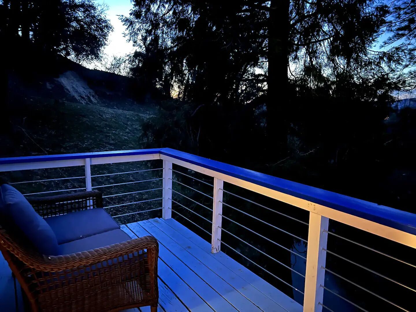A wooden deck with a white railing, a wicker chair, and a cushion.