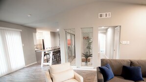 A spacious living room with a beige sofa, a brown sofa with blue cushions, and a white armchair. There is a dining area with a table and chairs visible through a glass door. - Full Family Stay Near At&t, Ballpark, 6 Flags & Airport (Grand Prairie)