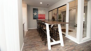 A dining area with a long wooden table and multiple chairs, a Texas flag mural on the wall, and a glass door leading to a balcony. - Full Family Stay Near At&t, Ballpark, 6 Flags & Airport (Grand Prairie)