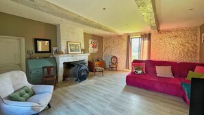 A living room with a fireplace, a red sofa, a white armchair, and a stone wall.
