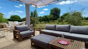 An outdoor patio with a wooden table, two cushioned chairs, a sofa, and a pergola.