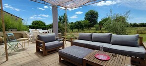 Un patio al aire libre con una mesa de madera, dos sillones con cojines, un sofá y una pérgola.