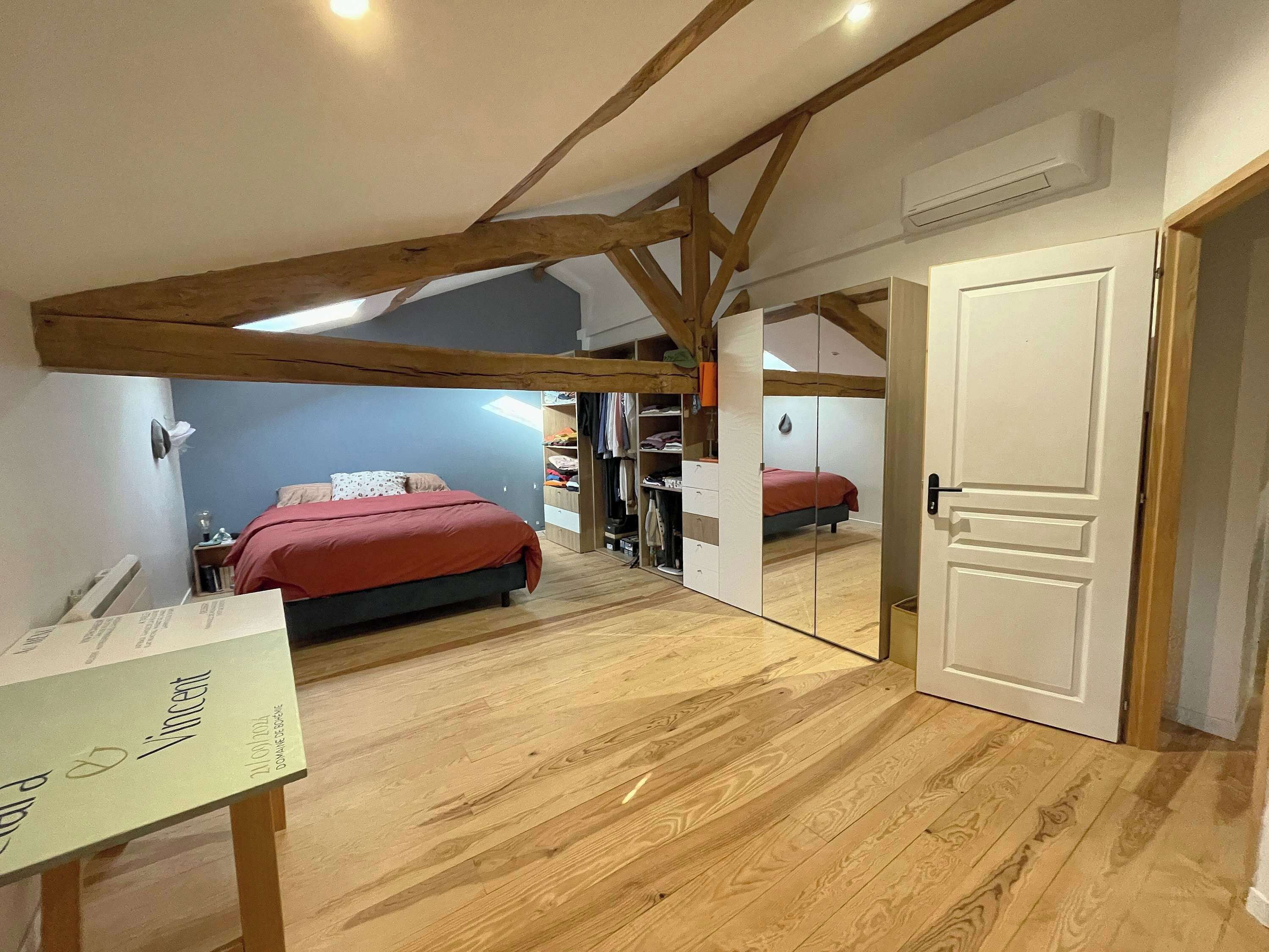 Un dormitorio con techo de madera, una cama con manta roja, un armario y una puerta.