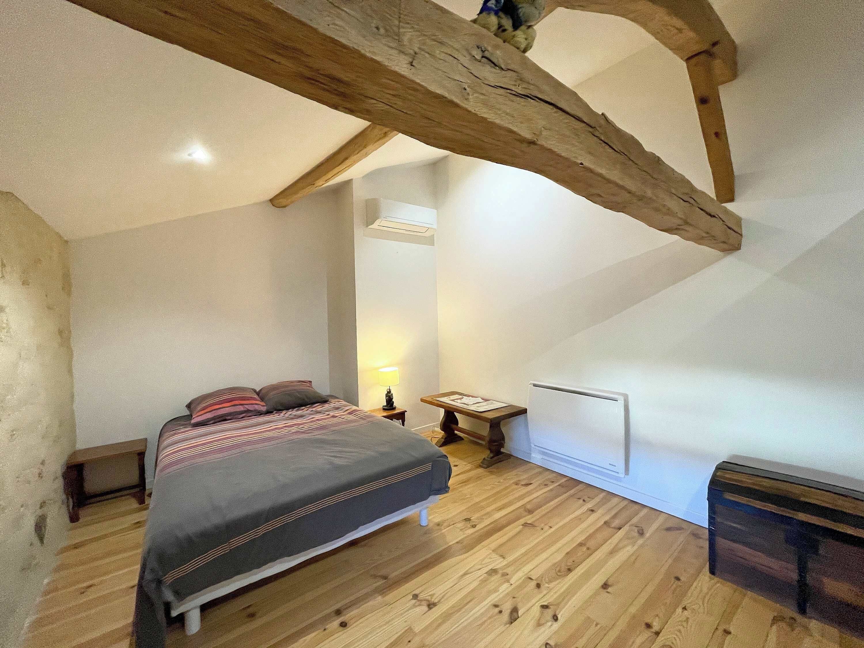 Een slaapkamer met een houten vloer, een bed met een gestreept dekbedovertrek, een nachtkastje met een lamp en een radiator.