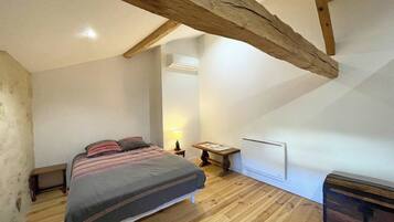 Een slaapkamer met een houten vloer, een bed met een gestreept dekbedovertrek, een nachtkastje met een lamp en een radiator.