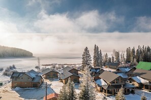 A snow-covered lodge with multiple buildings, a clear view of the surrounding forest, and a body of water in the distance. - Cabin # 2 - Lakeside cabin sleeps 11 with private hot tub (Naramata)