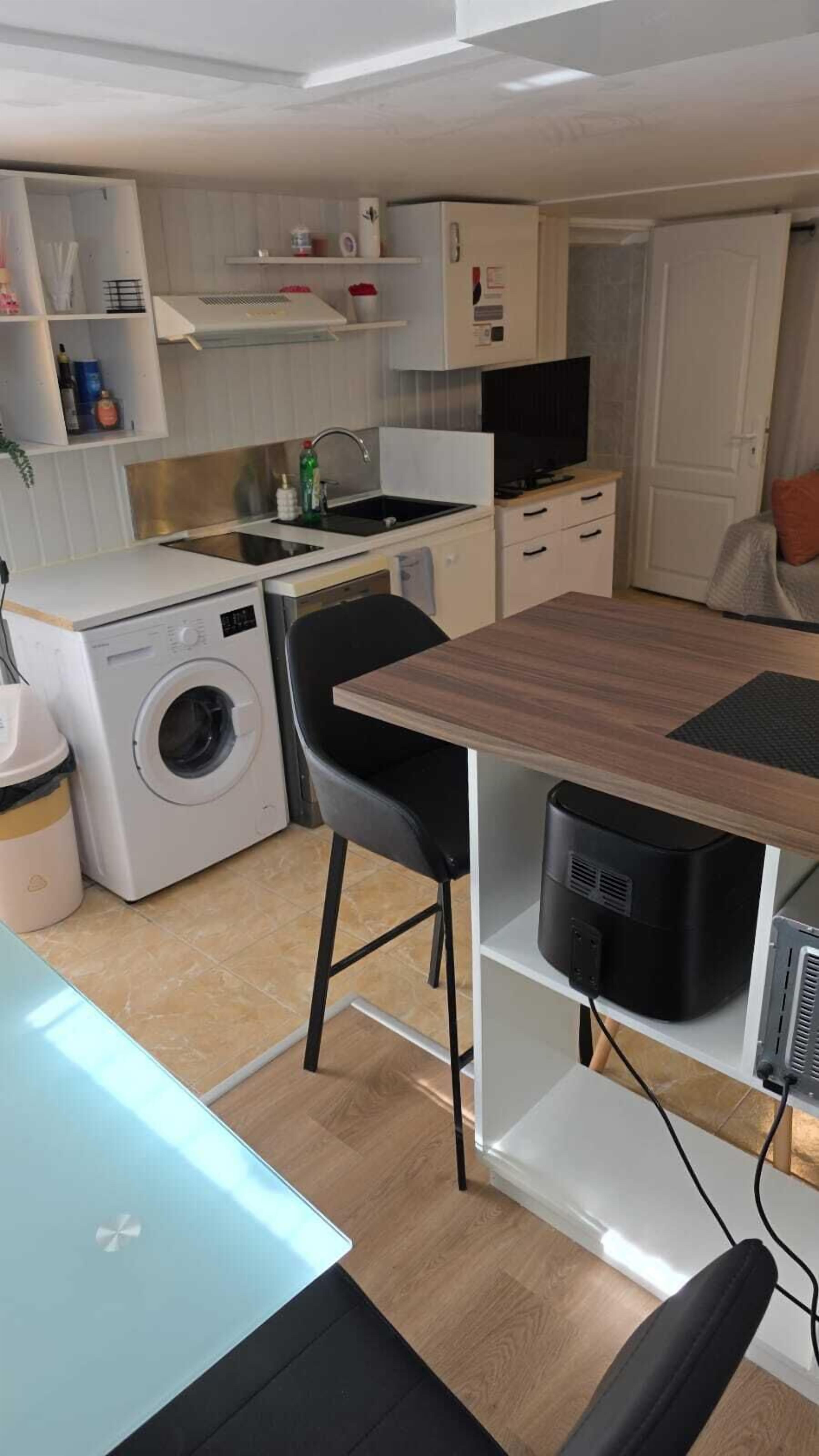 Une cuisine compacte équipée d’un lave-linge, d’un évier et d’un coin repas avec une table et des chaises.
