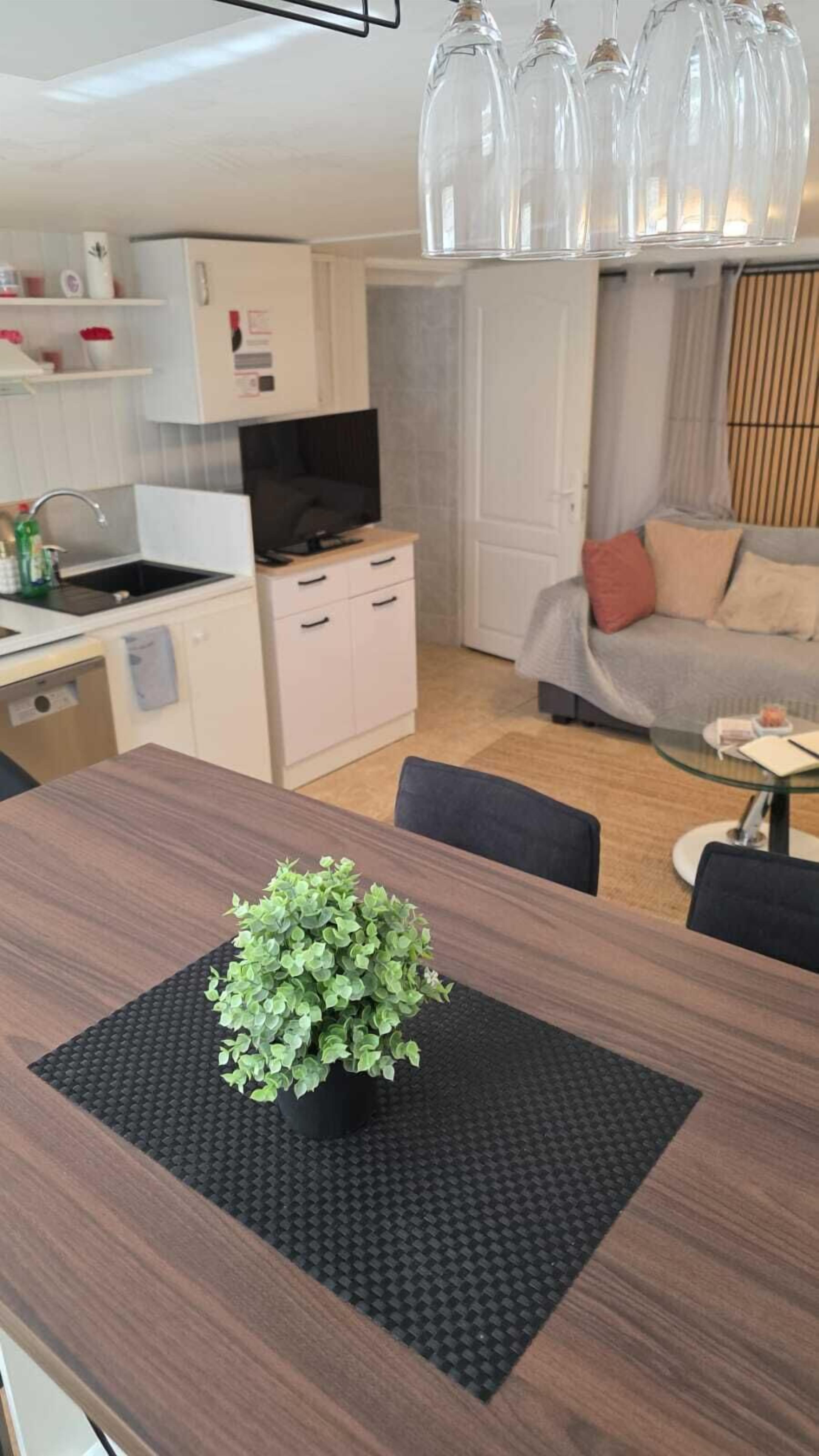 Ett modernt kök med vita skåp, en svart bänkskiva och ett matbord med en krukväxt.