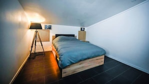 A modern bedroom with a single bed, a standing lamp, and a wall-mounted clock.