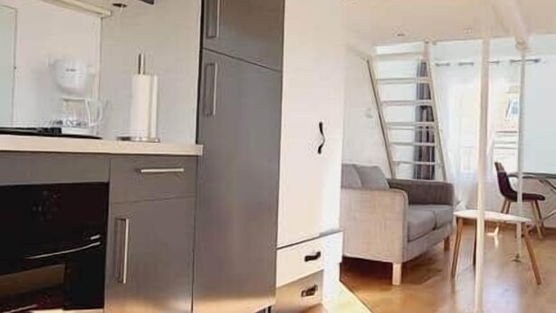 Una cocina moderna con electrodomésticos de acero inoxidable, una zona de comedor con mesa y sillas, y un altillo con escalera.