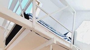 Un espacio tipo loft con techo alto, una escalera, un sofá y una zona de comedor.