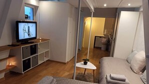 Un dormitorio moderno con cama, televisor mostrando un diseño de zapato, una mesita con una planta y un vestidor.