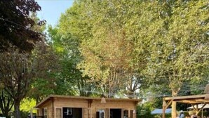 Una pequeña estructura de madera con asientos al aire libre, rodeada de árboles y un área verde.