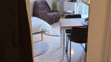 Un espace de vie compact comprenant un lit, une table à manger, un téléviseur et une petite plante.