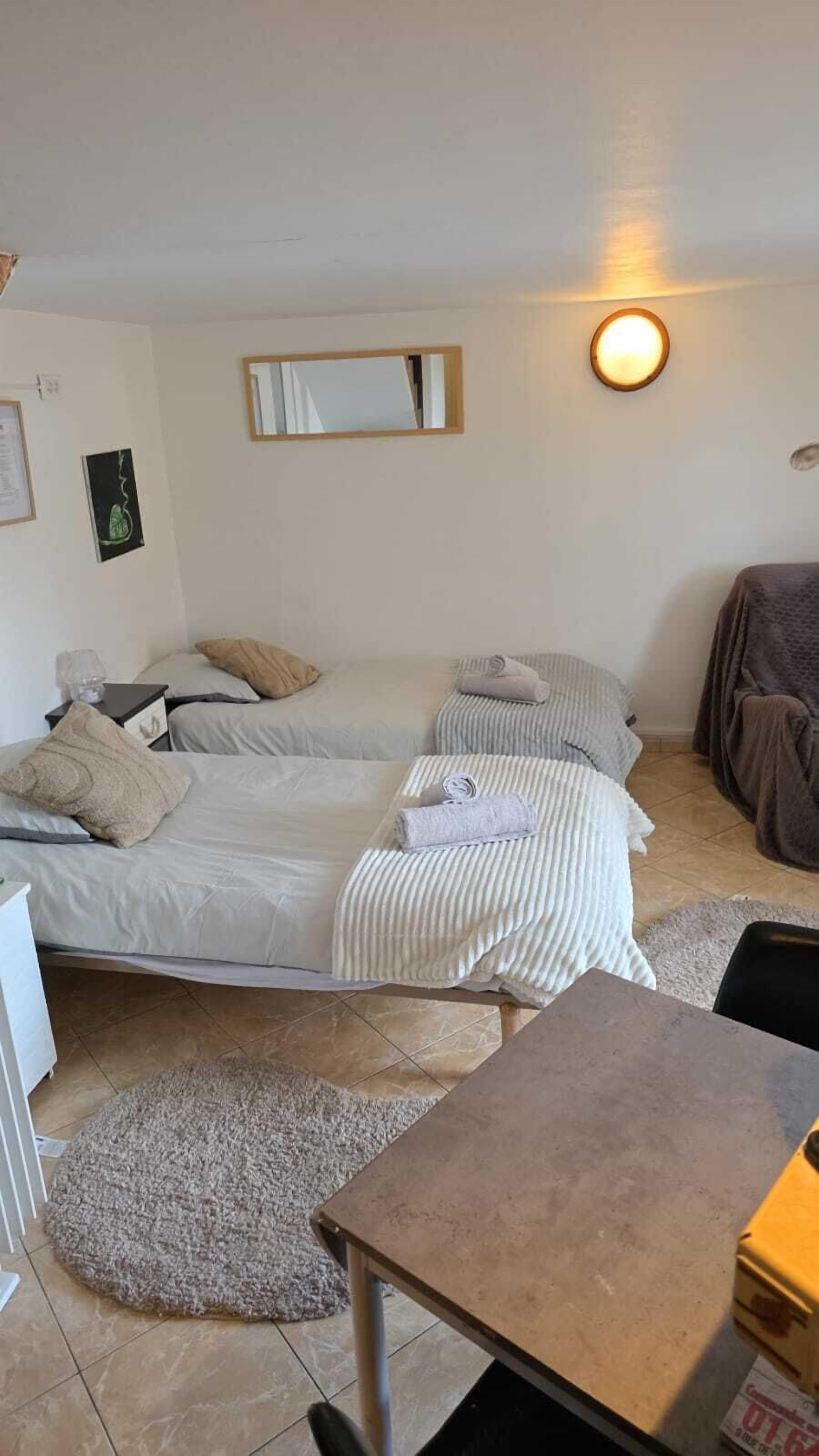 Una habitación con dos camas, una mesita, un espejo y una lámpara de pared.