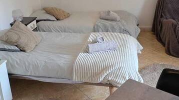 Una habitación con dos camas, una mesita, un espejo y una lámpara de pared.