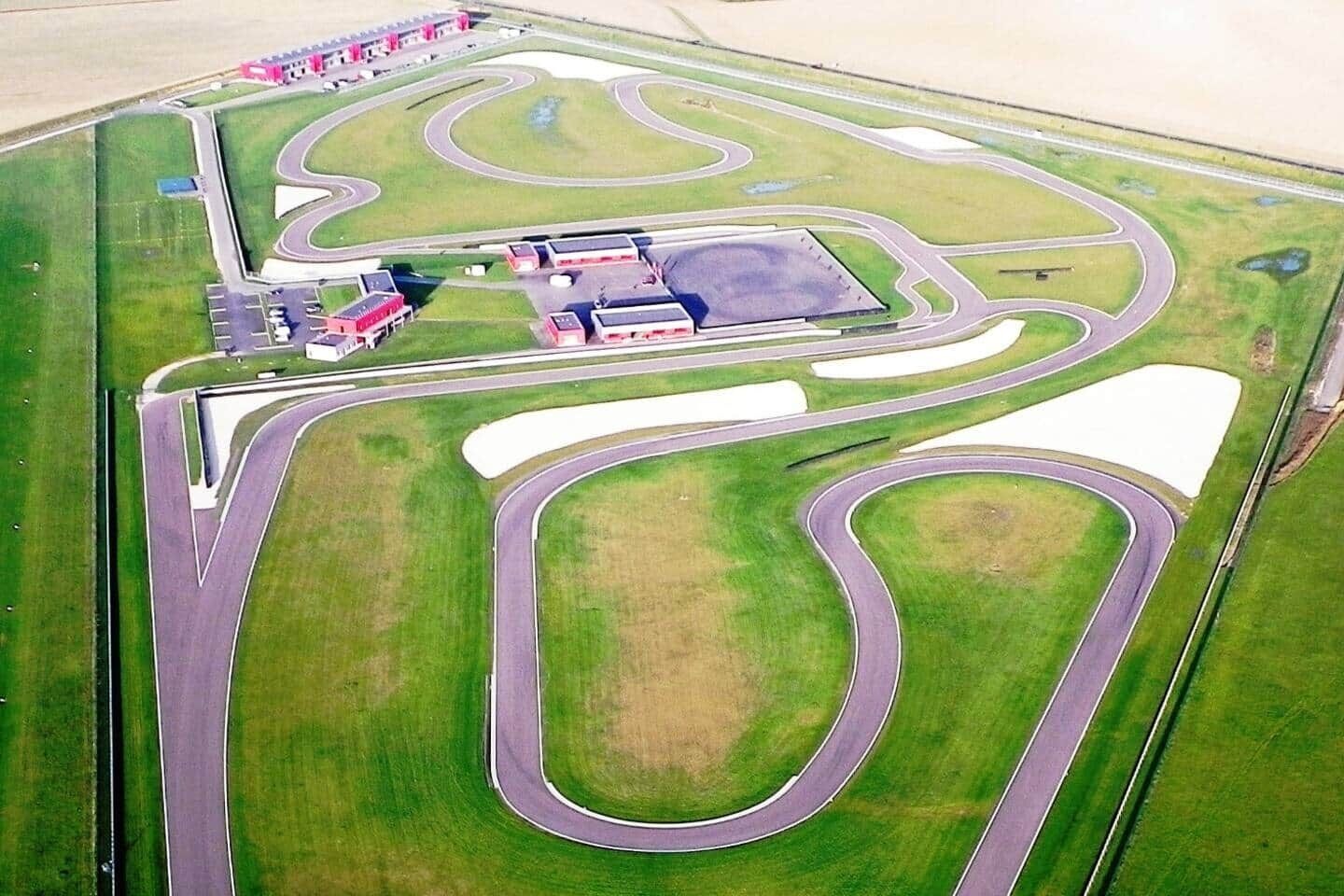 Une vue aérienne d’un circuit automobile comportant plusieurs pistes, une zone d’arrêt et un grand parking.