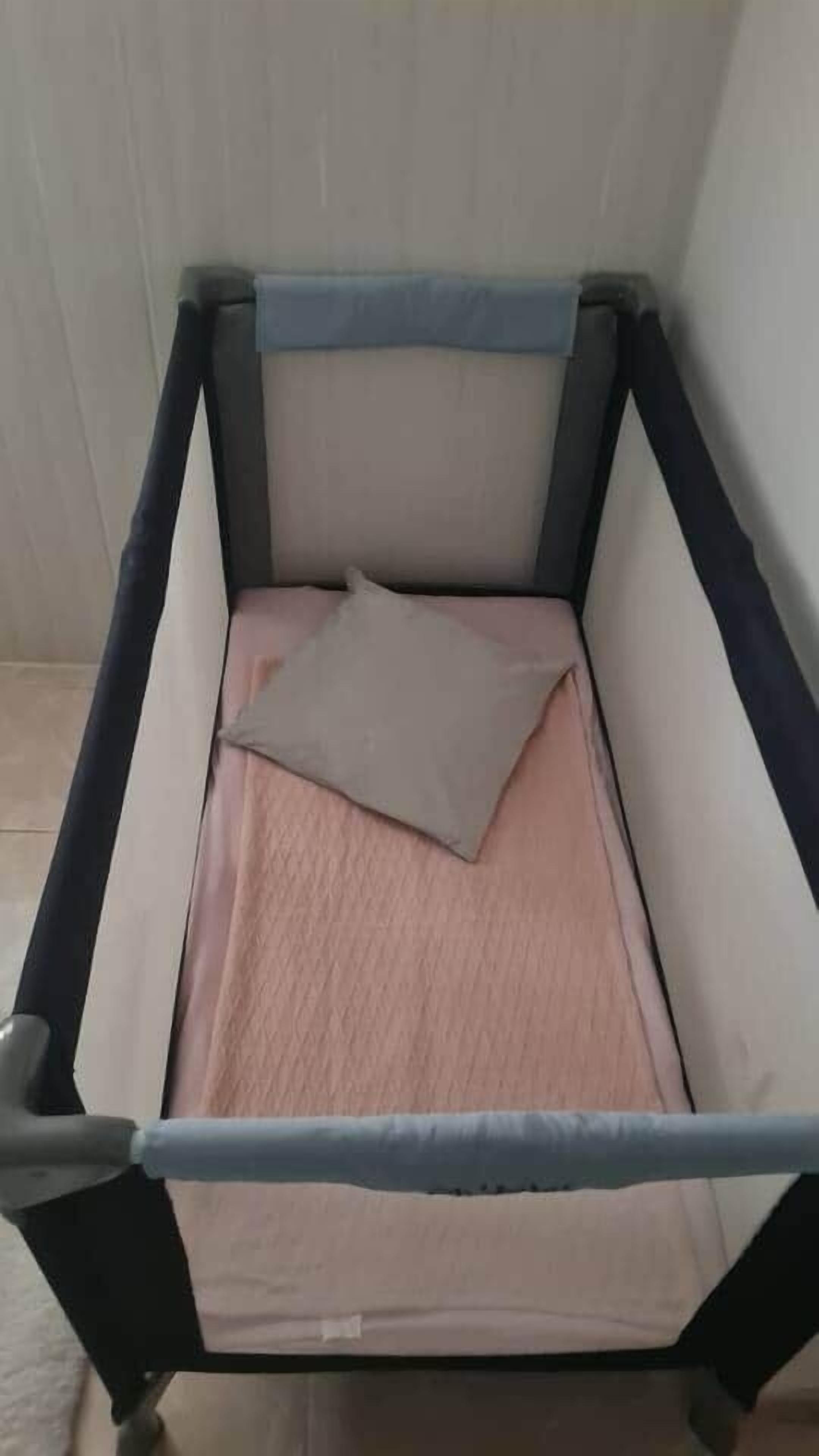 Ein kleines Bett mit einer Matratze und Kissen, umgeben von einem Metallrahmen.