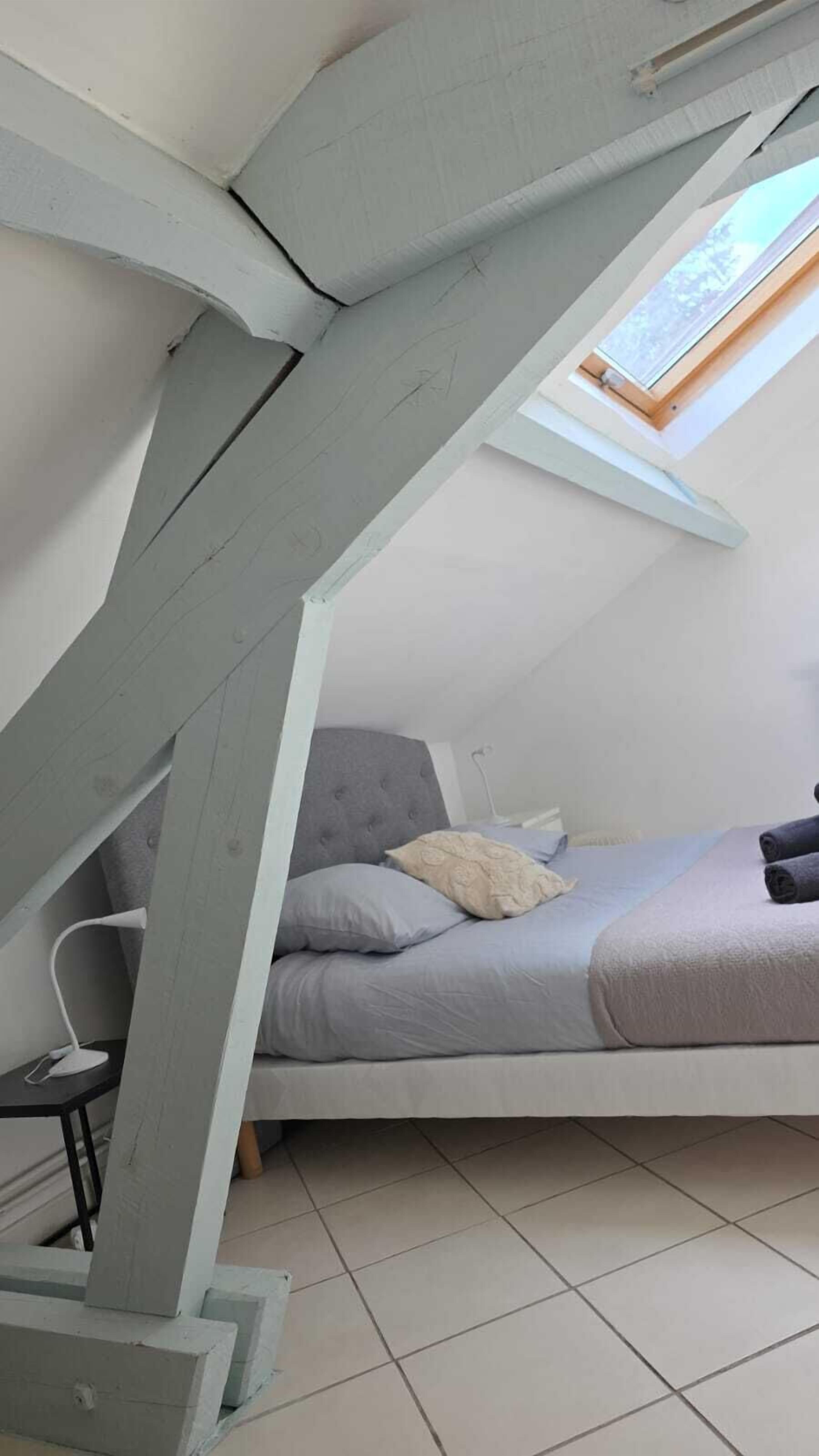 Una camera da letto con soffitto spiovente, un letto, un lucernario e una scrivania bianca con lampada.