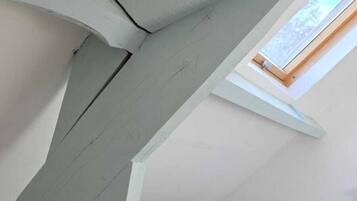 Una camera da letto con soffitto spiovente, un letto, un lucernario e una scrivania bianca con lampada.