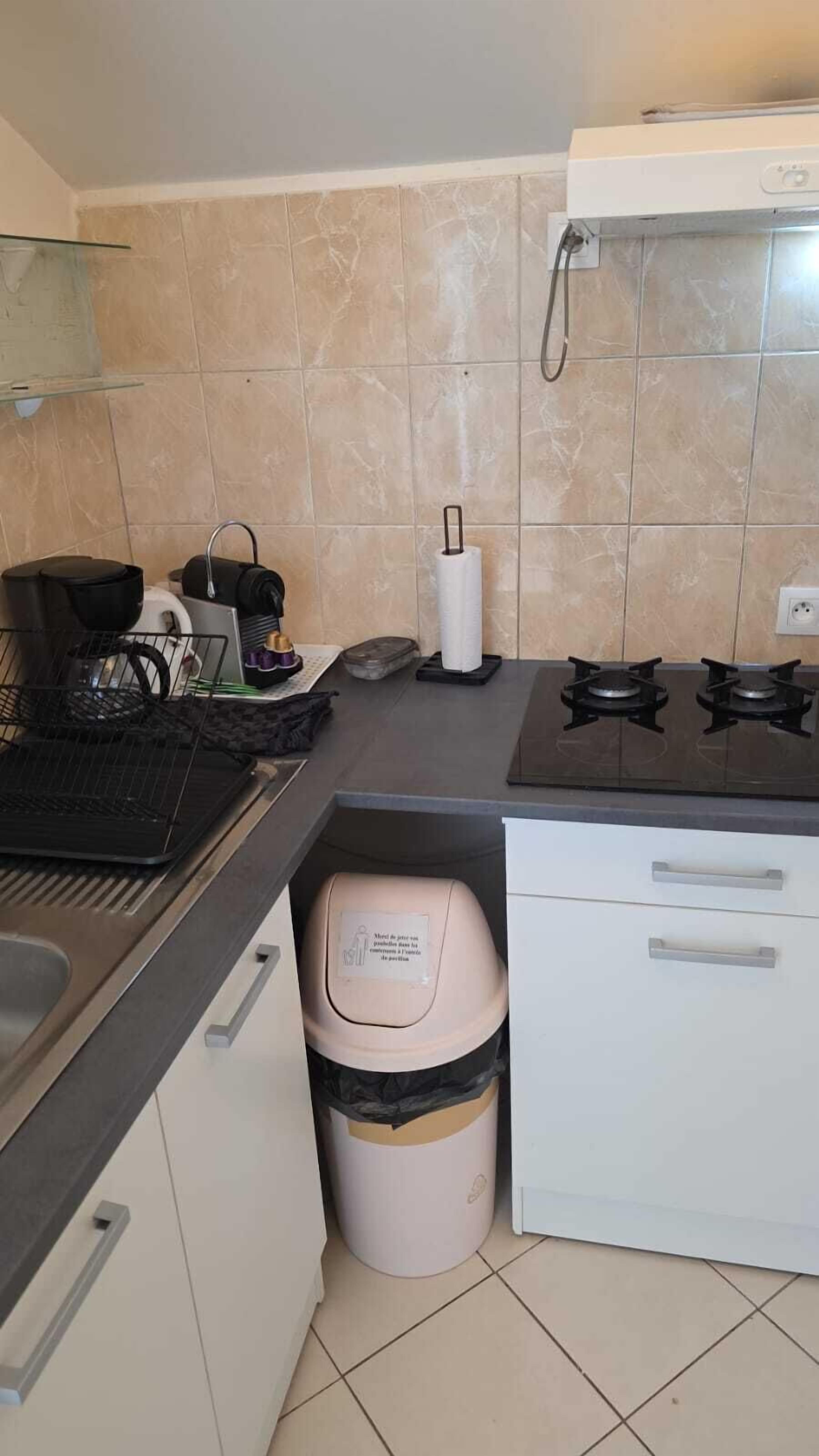 A kitchen with a gas stove, a sink, a trash bin, and a countertop with various items.