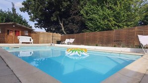 A rectangular swimming pool with a floating inflatable toy, surrounded by a wooden fence and white lounge chairs.