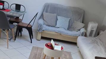 A compact living space with a dining area, a sofa, a small table with a laptop, and a ceiling fan.